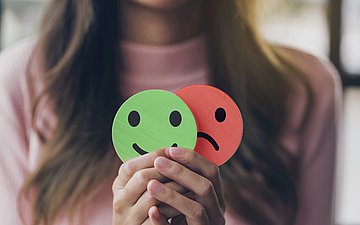 Lachender und weinender Smiley Foto: Eine Frau hält in ihren Händen zwei Symbole – eines zeigt einen lachenden, das andere einen weinenden Smiley.