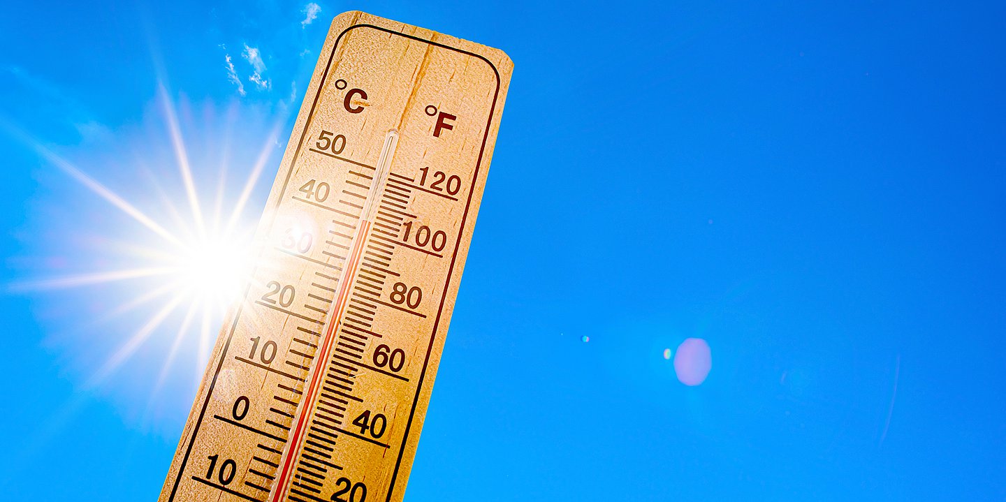 Foto: Ein Hitzebarometer ragt in den blauen Himmel und wird von der Sonne angestrahlt.