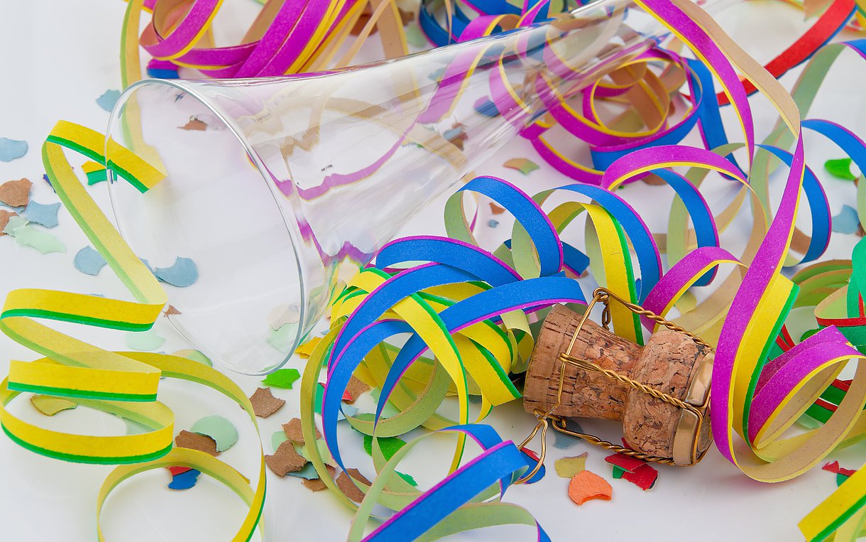 Symbolbild Fasching: Ein umgekipptes, leeres Sektglas liegt zwischen bunten Luftschlangen aus Papier.