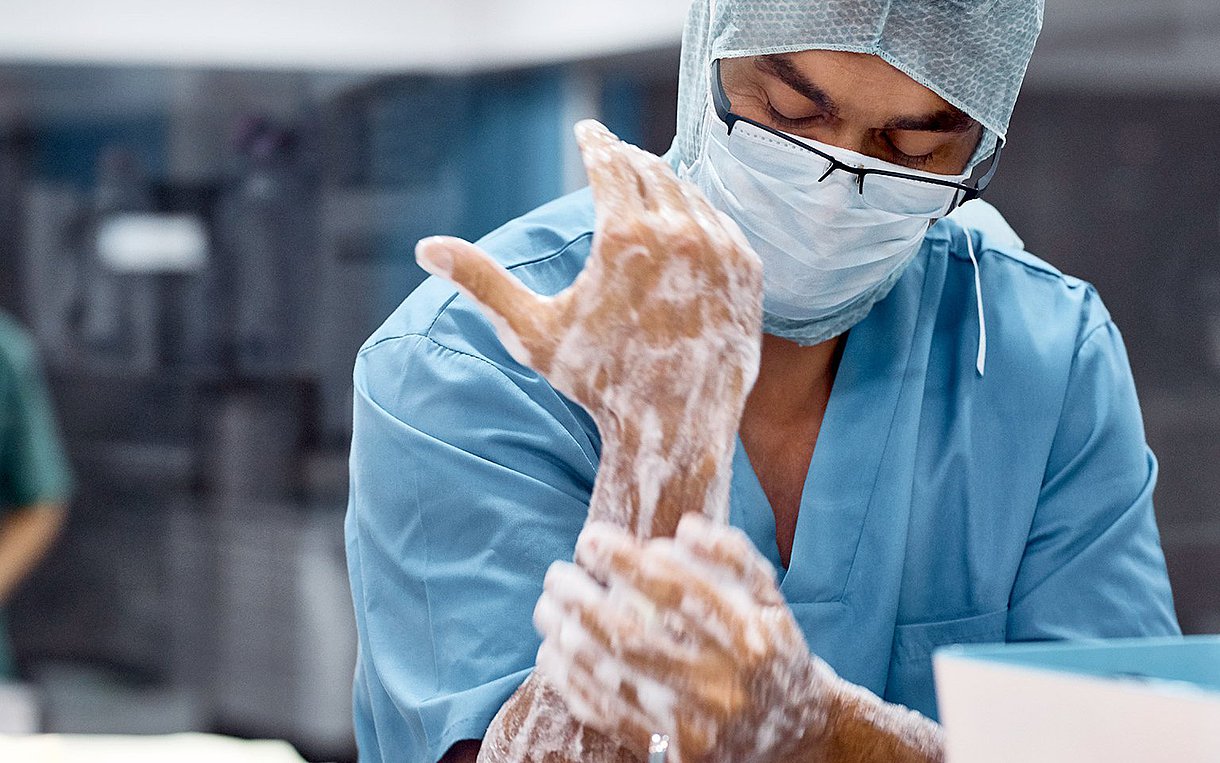 Arzt in OP-Kleidung wäscht sich vor der OP mit der linken Hand den rechten Arm