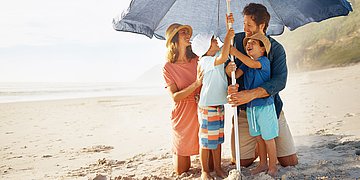 Sonnenschutz Eine Familie am Strand stellt einen Sonnenschirm auf.