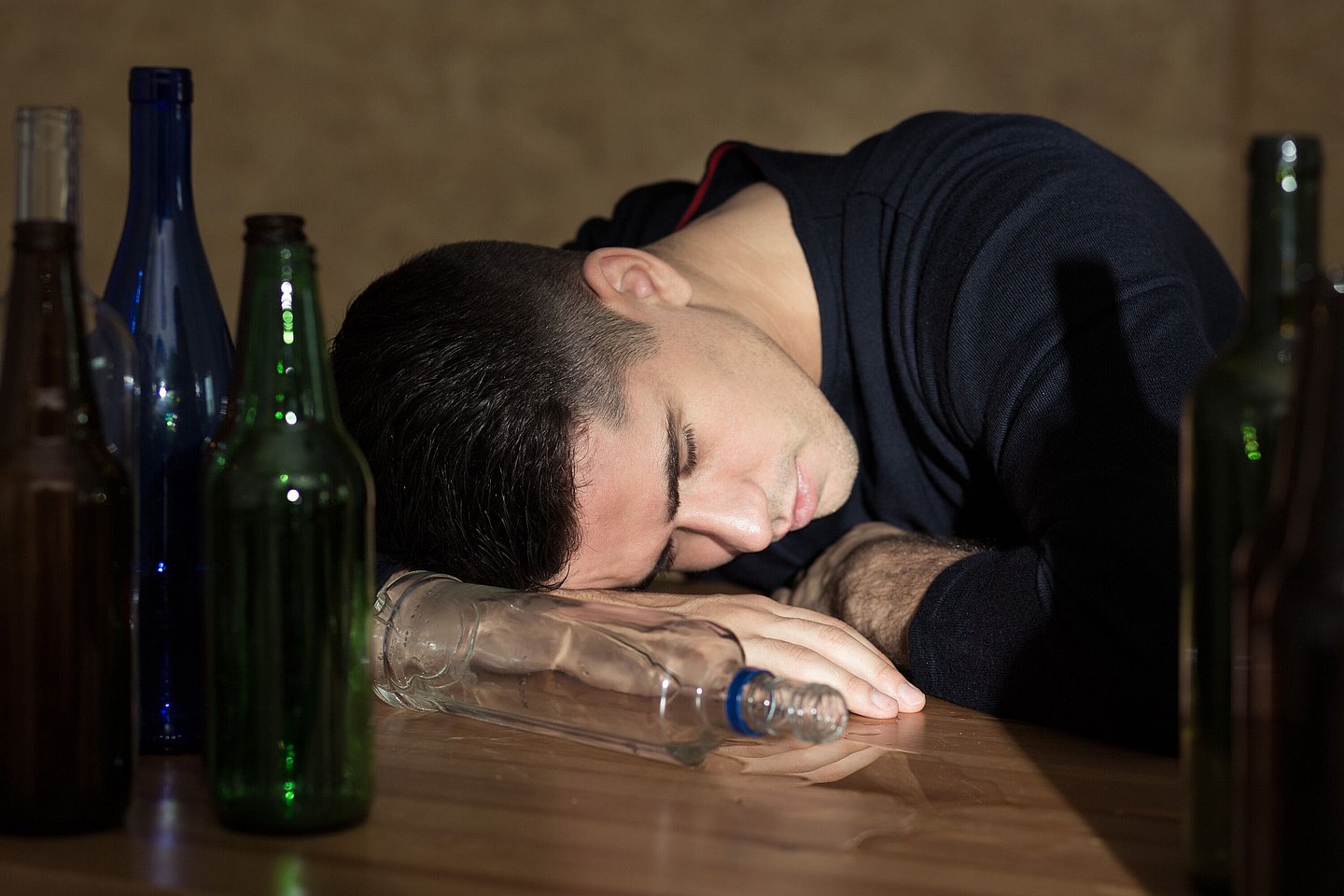 Ein Jugendlicher liegt schlafend auf einem Tisch mit leergetrunkenen Flaschen.