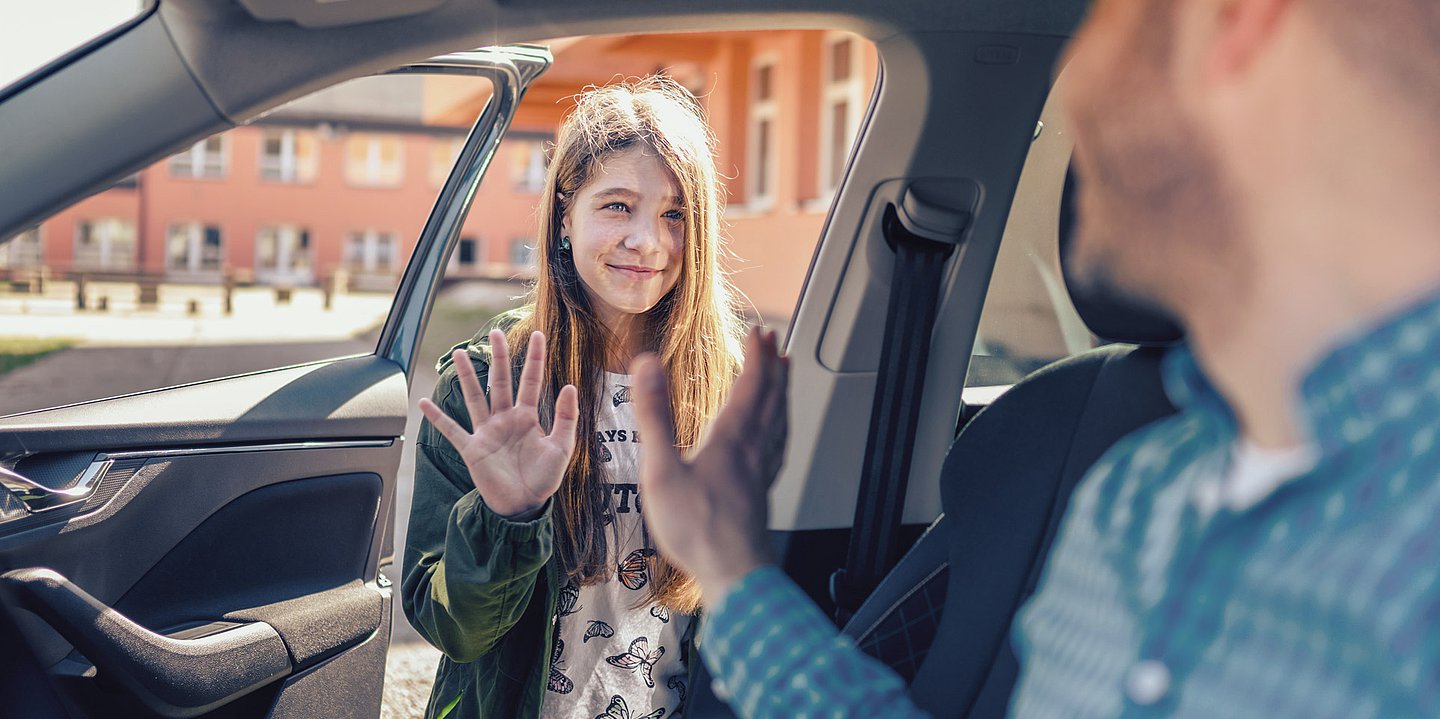Foto: Ein Mädchen verabschiedet sich an der offenen Autotüre von ihrem Vater.