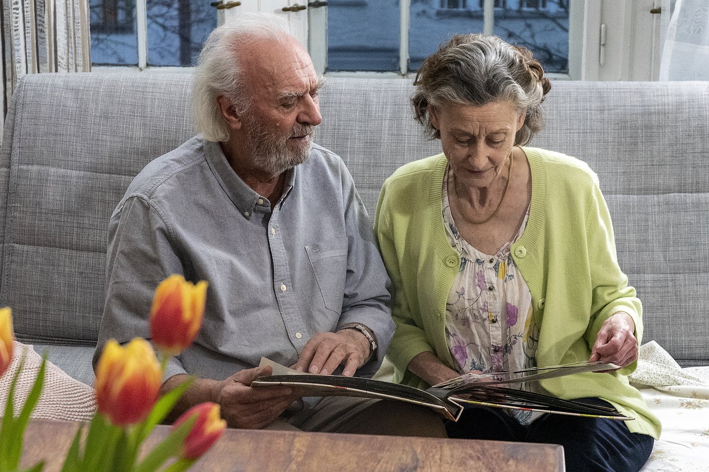 Foto: Ein älterer Mann und eine ältere Frau sitzen auf einem Sofa und schauen sich ein Fotoalbum an.