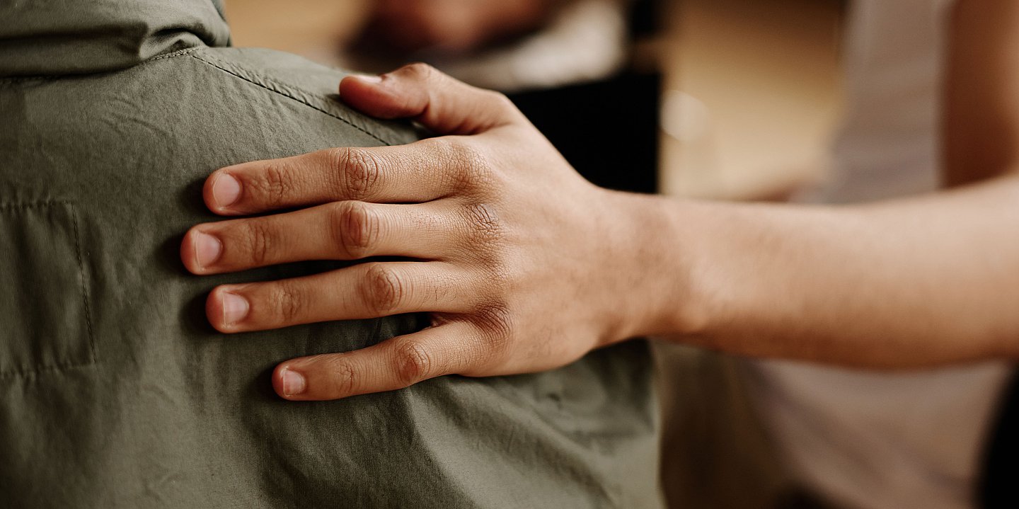 Foto: Die Hand eines Menschen fasst an die Schulter eines anderen.