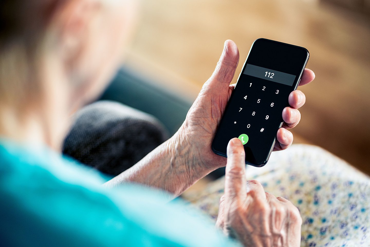 Eine sitzende ältere Frau im Schlafanzug hält ein Handy in der Hand und drückt gerade den Notruf 112.