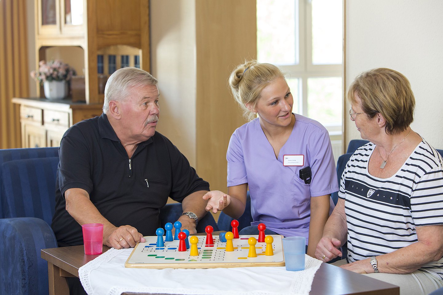 Foto: Eine Pflegerin spielt Gesellschaftsspiele mit zwei Pflegebedürftigen.