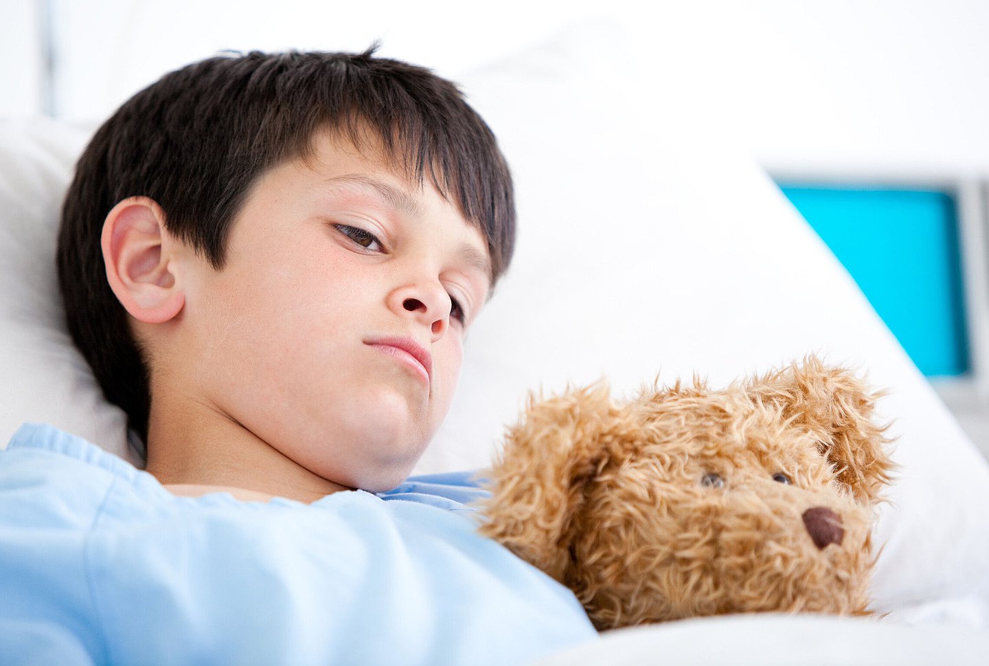 Ein Junge liegt mit seinem Teddy in einem Krankenhausbett.