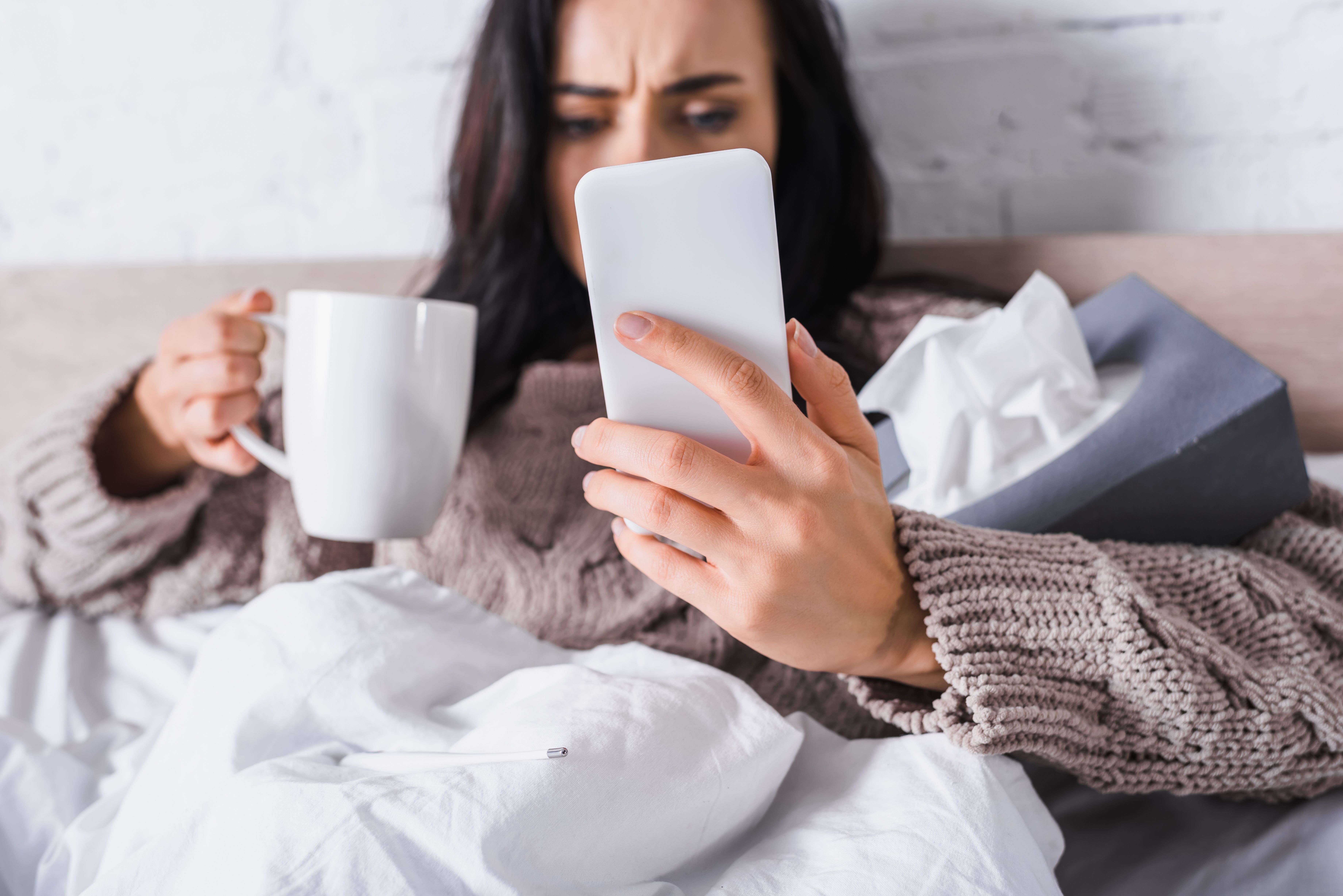 Frau mit Tee und Telefon im Bett