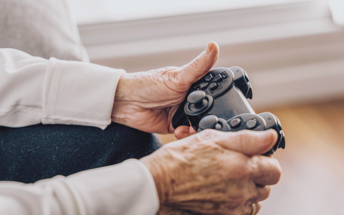 Foto: Zwei Hände eines älteren Menschen halten eine Spielkonsole in der Hand.