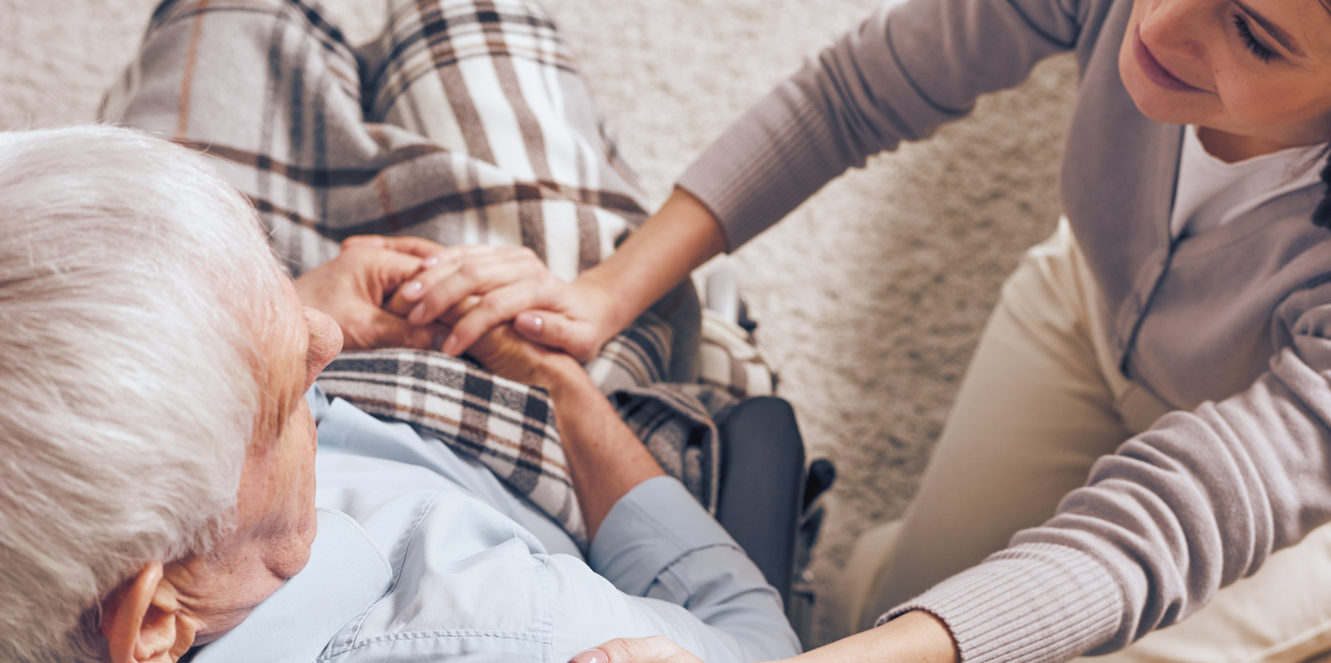 Foto: Eine jüngere Frau sitzt neben einem älteren Mann und hält seine Hand.