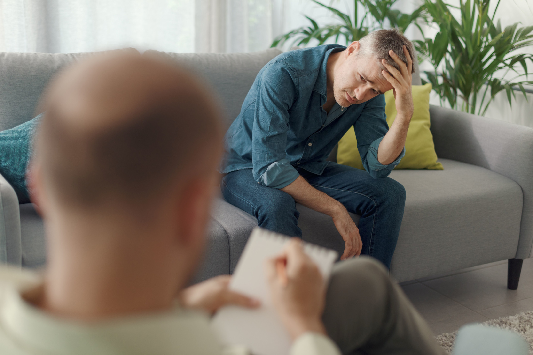 Das Foto zeigt einen Mann auf einer Couch sitzend im Gespräch mit seinem Psychotherapeuten.