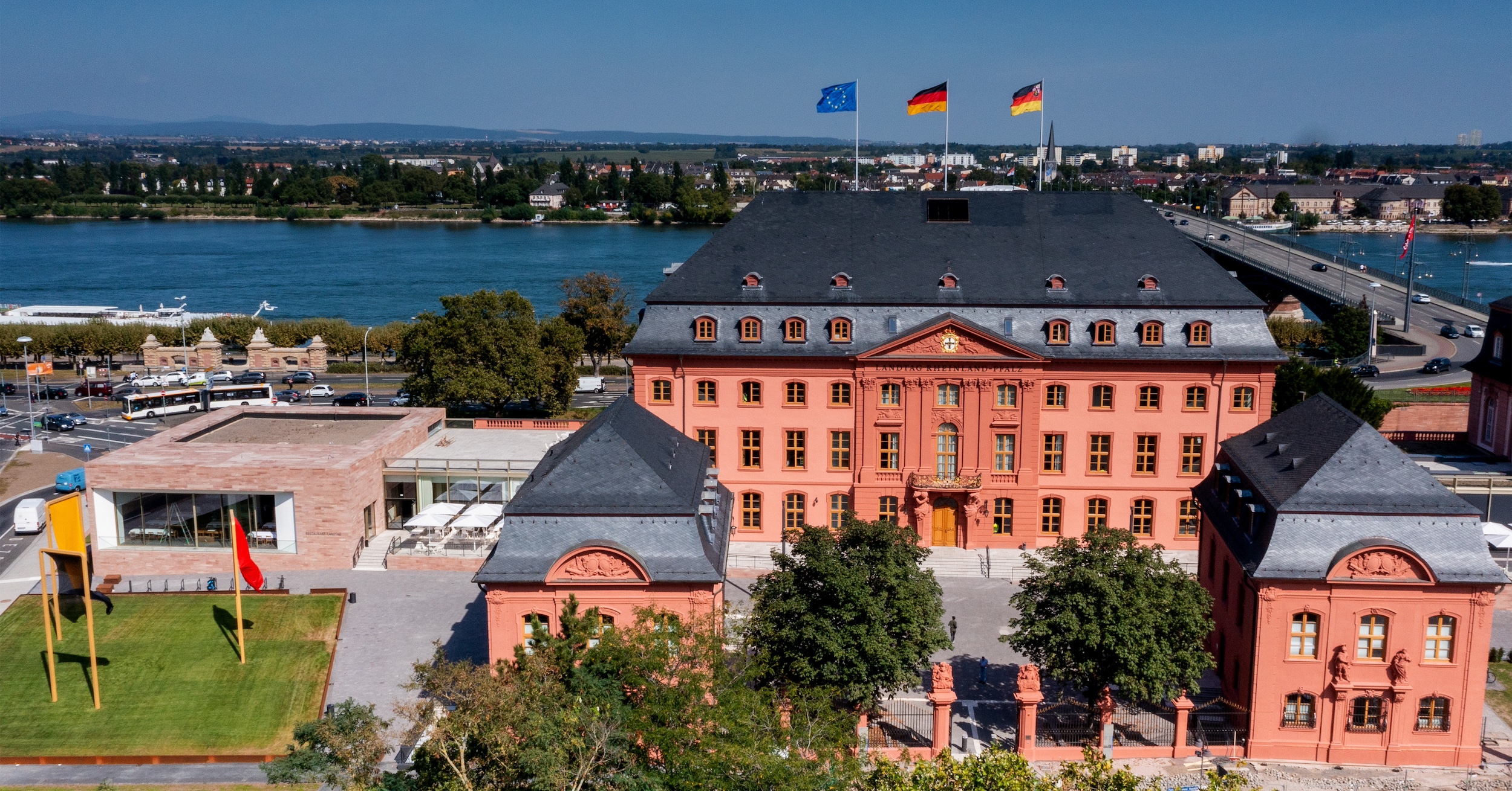 Foto zeigt den Blick auf das historische rotbraune Gebäude im Hintergrund fließt der Rhein