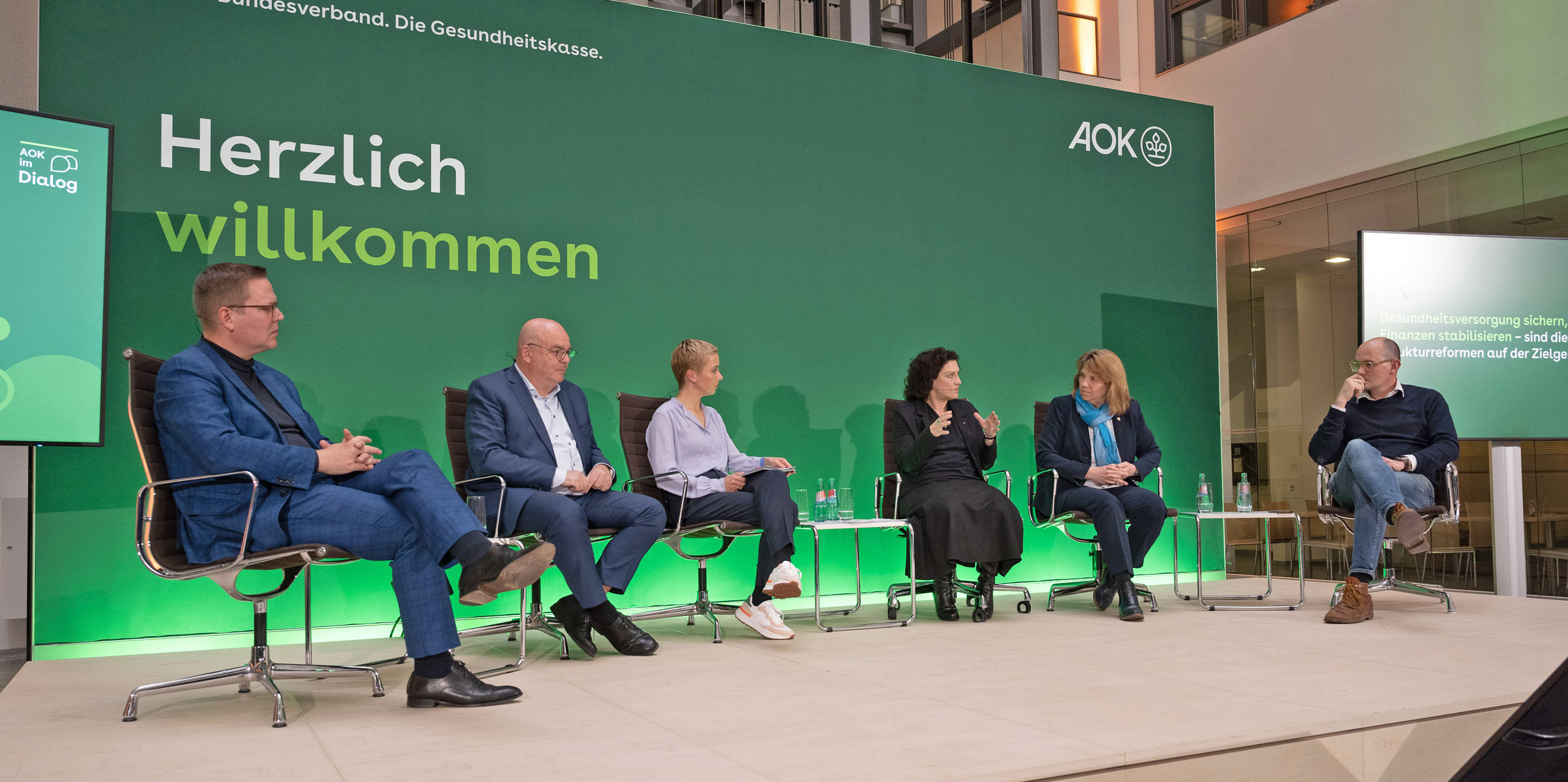 Das Foto zeigt Tino Sorge, Prof. Dr. Edgar Franke, Sarah Oswald, Dr. Carola Reimann, Prof. Dr. Kerstin von der Decken, Dr. Janosch Dahmen (v.l.) auf dem Podium einer Diskussionsveranstaltung im Atrium des AOK-Bundesverbandes