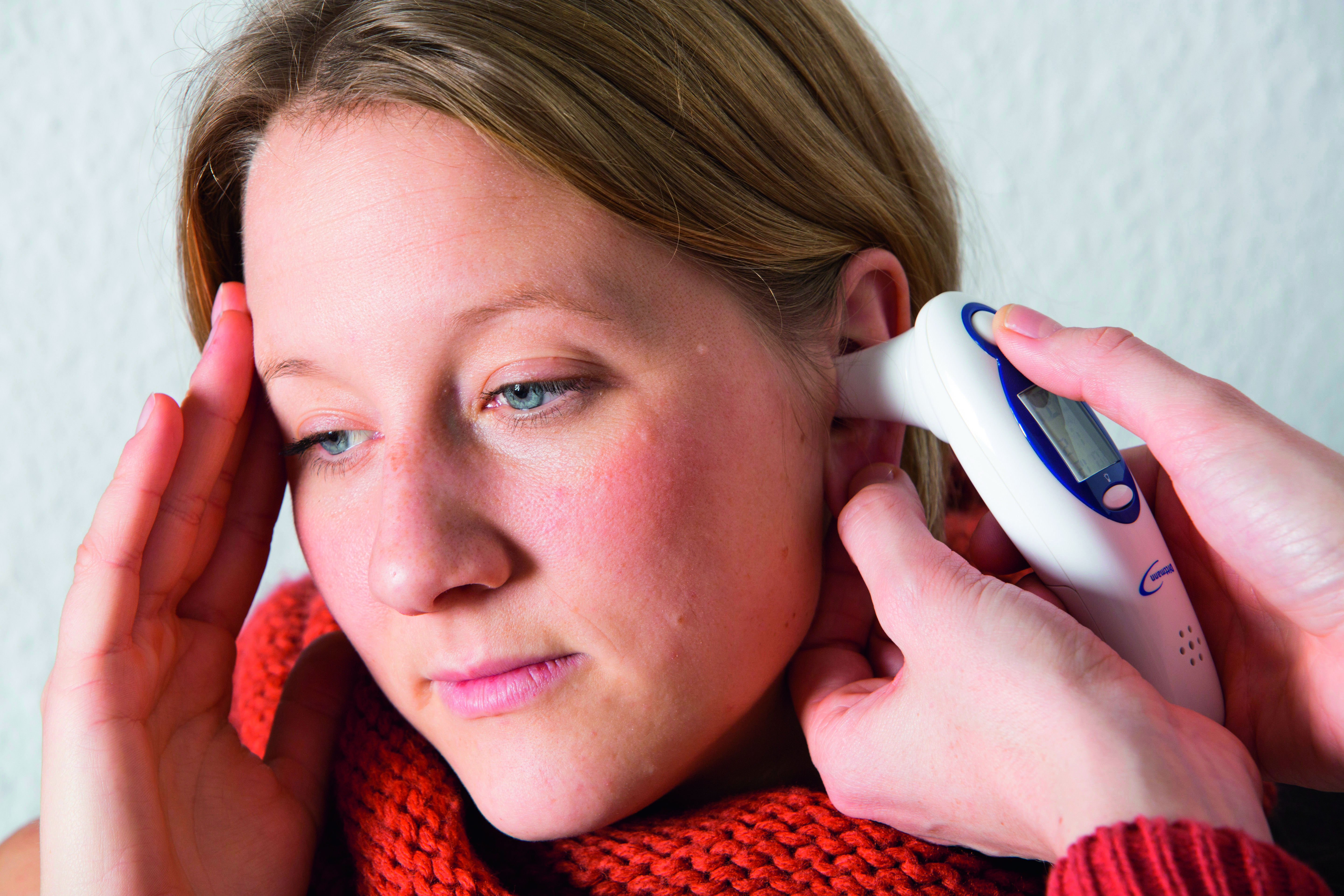 Foto: Bei einer jungen Frau wird das Fieber mit einem Ohrthermometer gemessen.