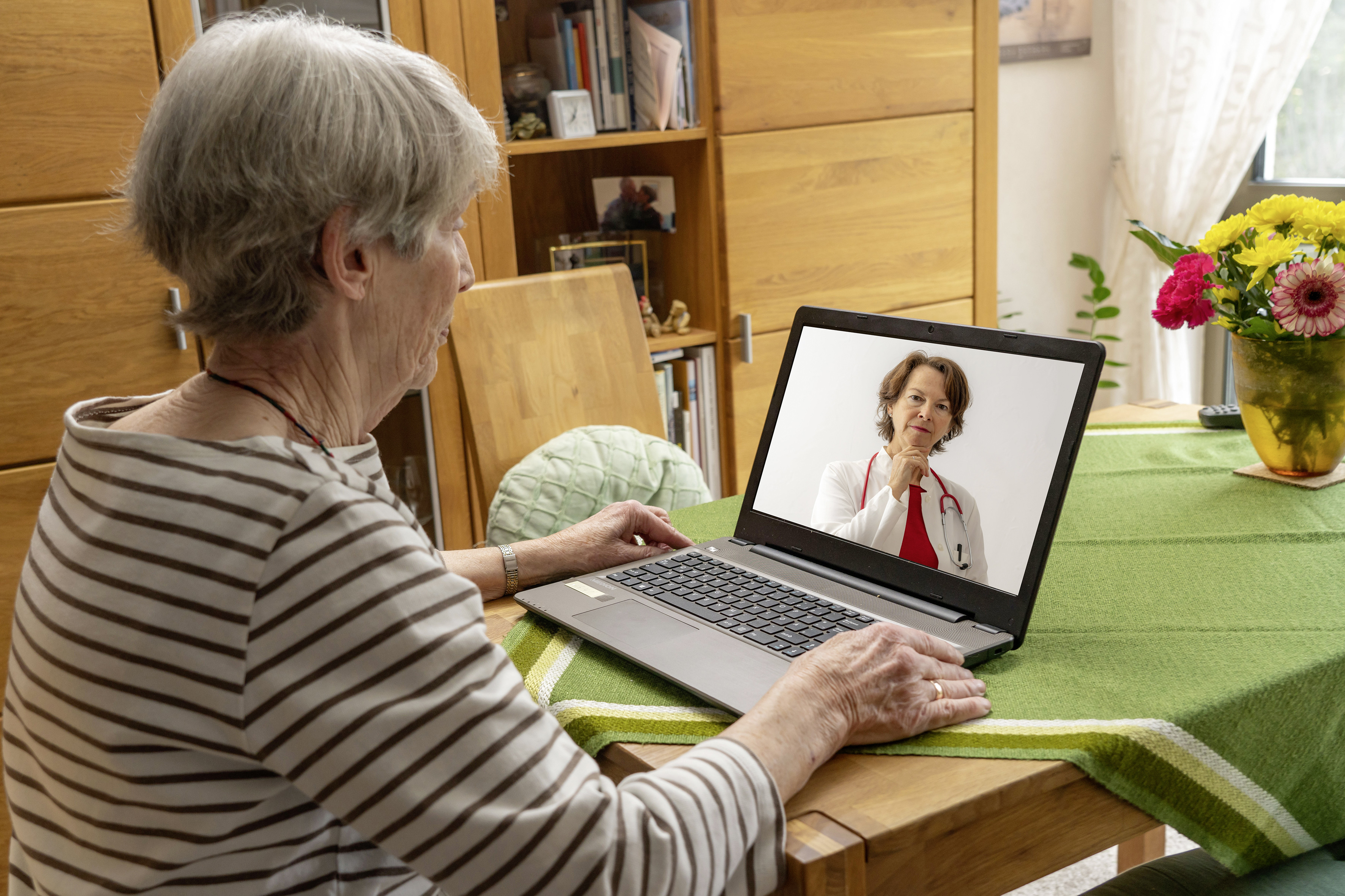 Foto: Eine ältere Dame ist bei einer Videosprechstunde zu Hause am Laptop.