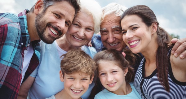 Sechs Personen aus drei Generationen, die sich in den Armen liegen und in die Kamera lächeln.