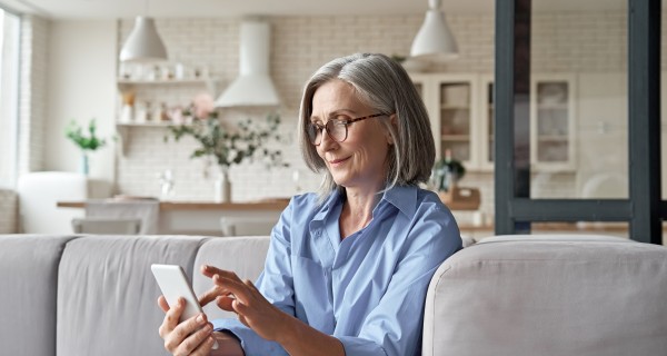 Eine Frau sitzt auf einer Couch und schaut zufrieden auf ein Mobiltelefon.