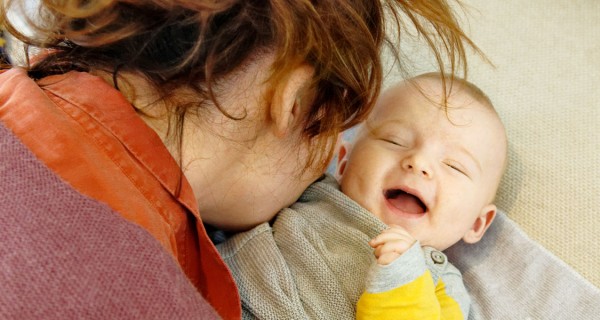 Eine Frau pustet einem lachenden Baby auf die Brust.