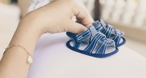 Ein Paar Babyschuhe werden auf einen Schwangerschaftsbauch gehalten.