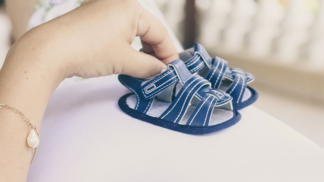 Ein Paar Babyschuhe werden auf einen Schwangerschaftsbauch gehalten.